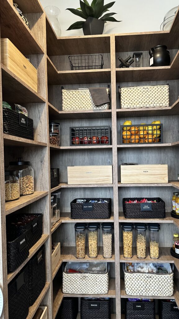 Modern organized pantry with labeled baskets, wooden boxes, and clear food containers