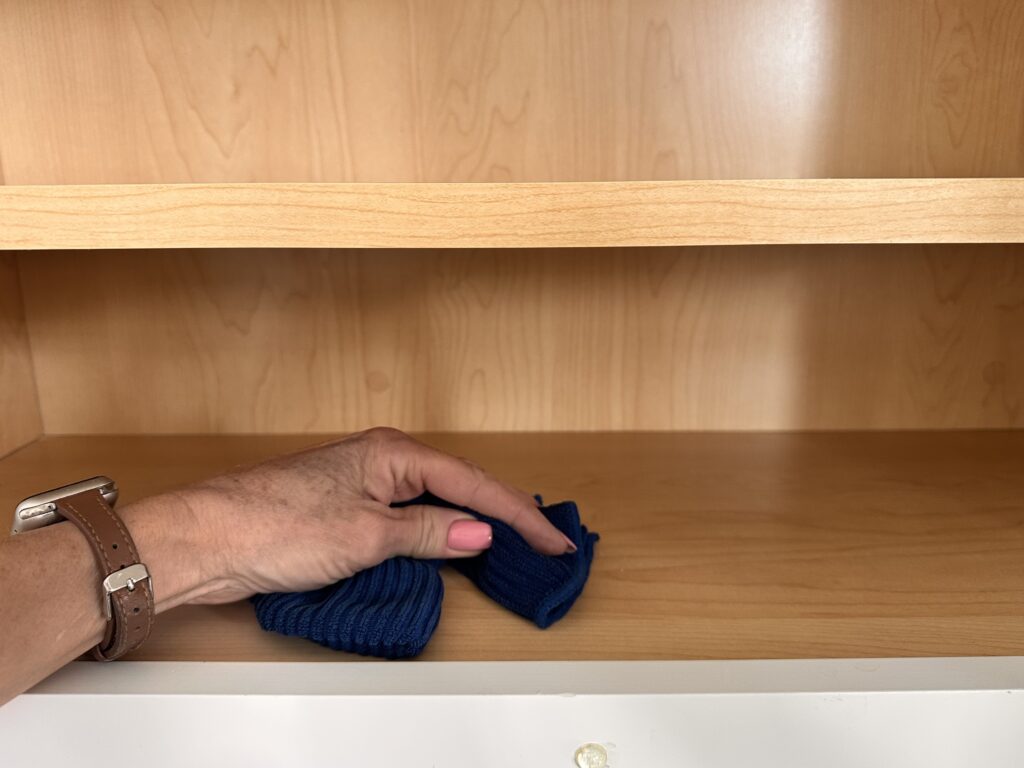 Hand wiping down a wooden shelf with a blue cloth during move-in cleaning