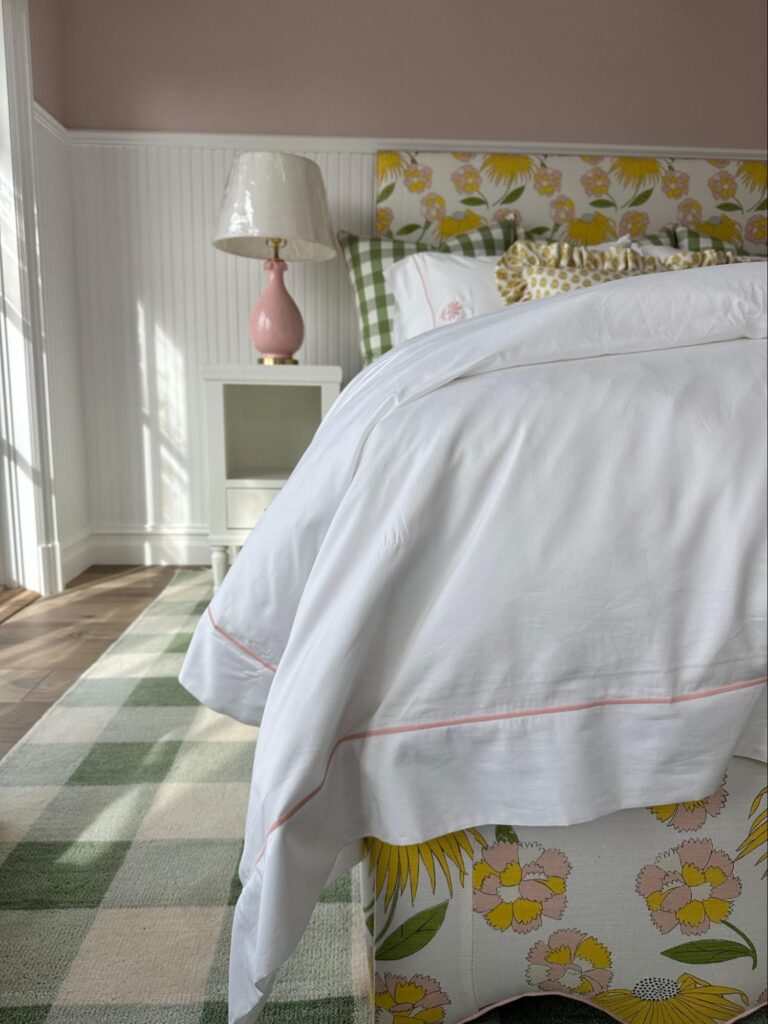 Sunlit bedroom with white bedding, nightstand, and soft floral accents.