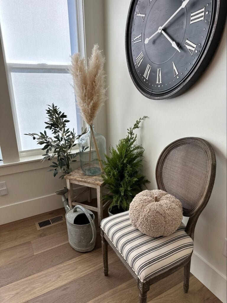 Cozy corner with chair, plants, wall clock, and decorative accents near a window.