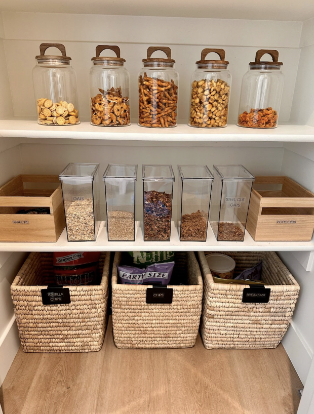 Pantry shelves with labeled jars, clear canisters of oats and granola, and woven baskets for snacks and chips.