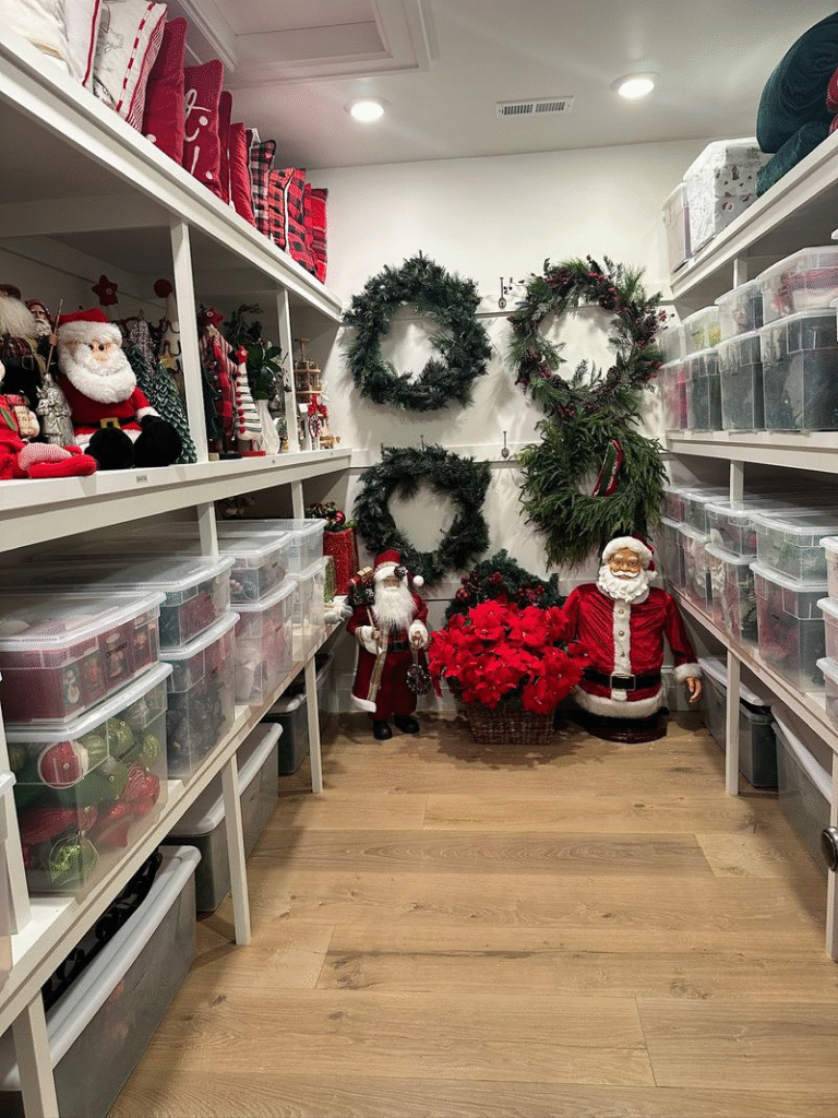 Storage room with wreaths hung on the back wall and rows of clear bins filled with holiday decorations.