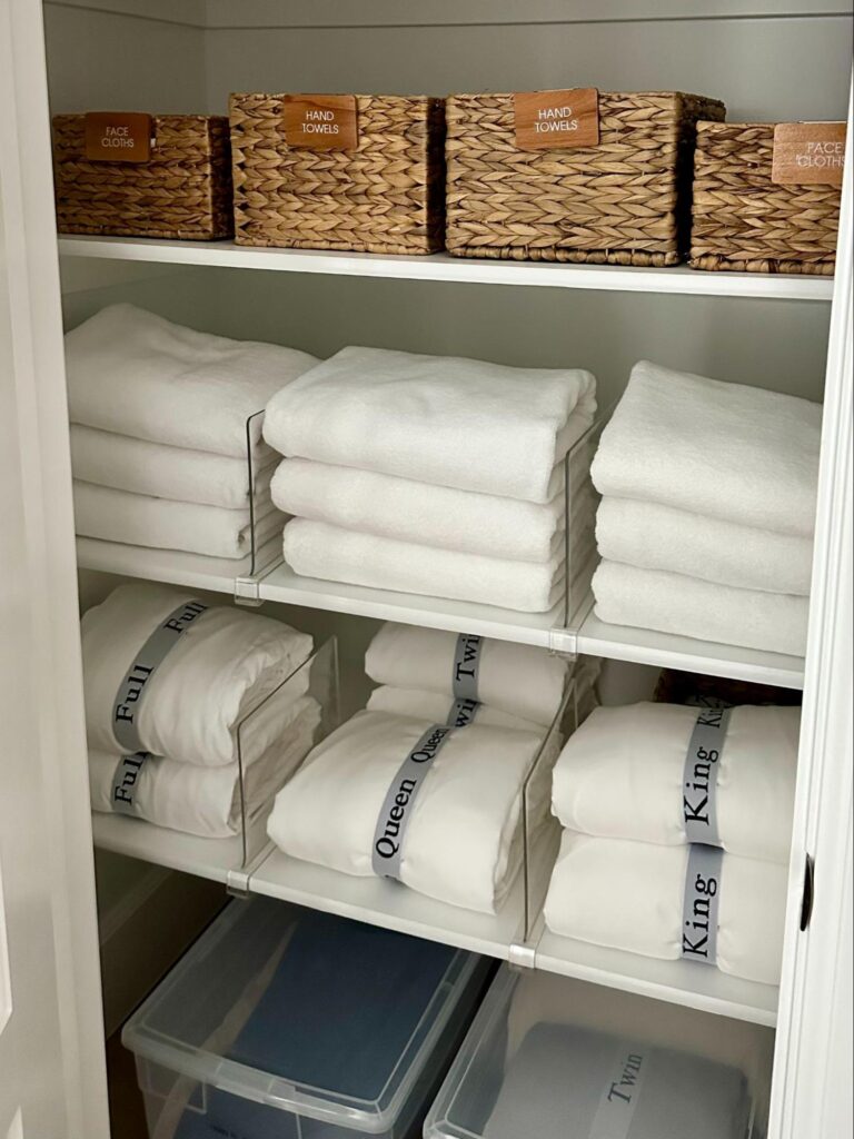 Organized linen closet with labeled baskets, folded towels, and neatly stored bedding.