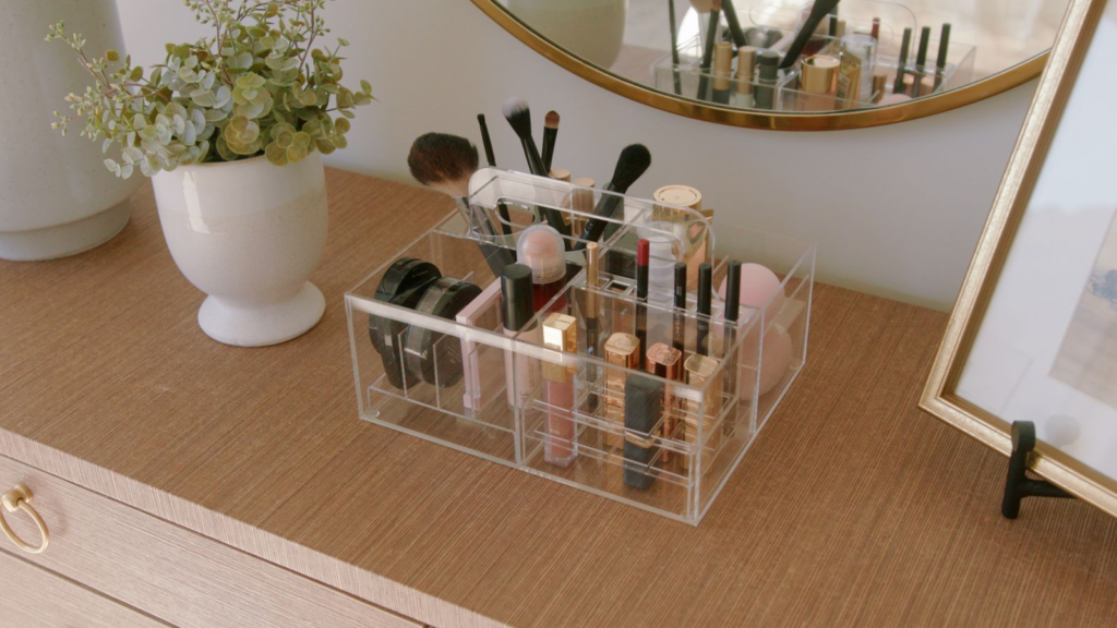 Bathroom organization ideas - Home Organization Clear acrylic makeup organizer on a vanity holding brushes, lipsticks, and cosmetics beside a mirror and plant