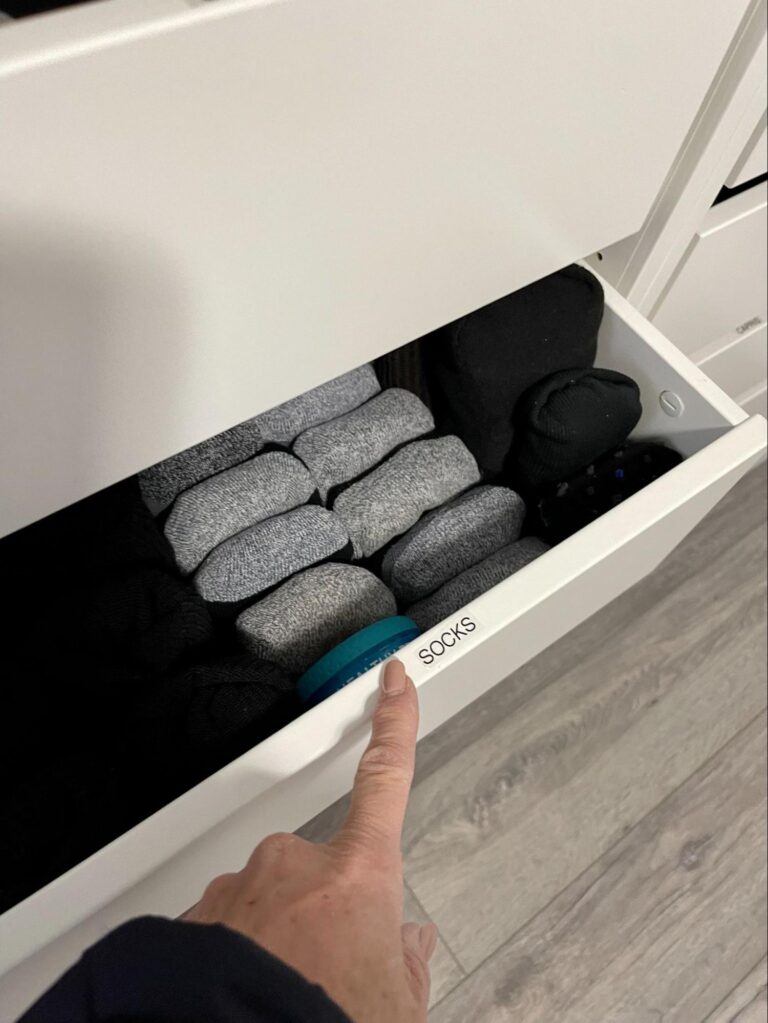 Drawer labeled socks with neatly folded pairs arranged by color, showing an organized and easy-to-maintain storage system