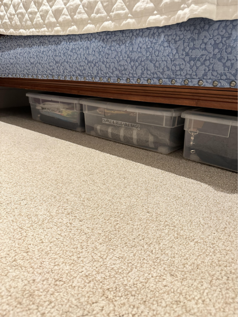 Clear storage bins neatly arranged under a bed, creating organized hidden storage in a master bedroom