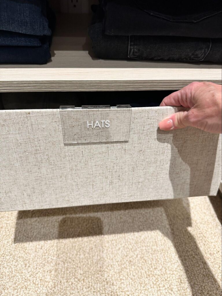 Labeled fabric drawer for hats being pulled open, showing an organized storage system inside a bedroom or closet