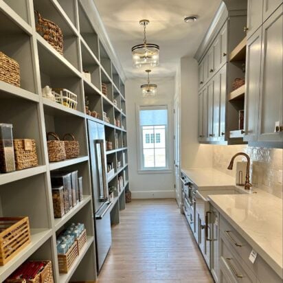 Organized pantry with open shelving, woven storage baskets, labeled containers, and a long countertop workspace