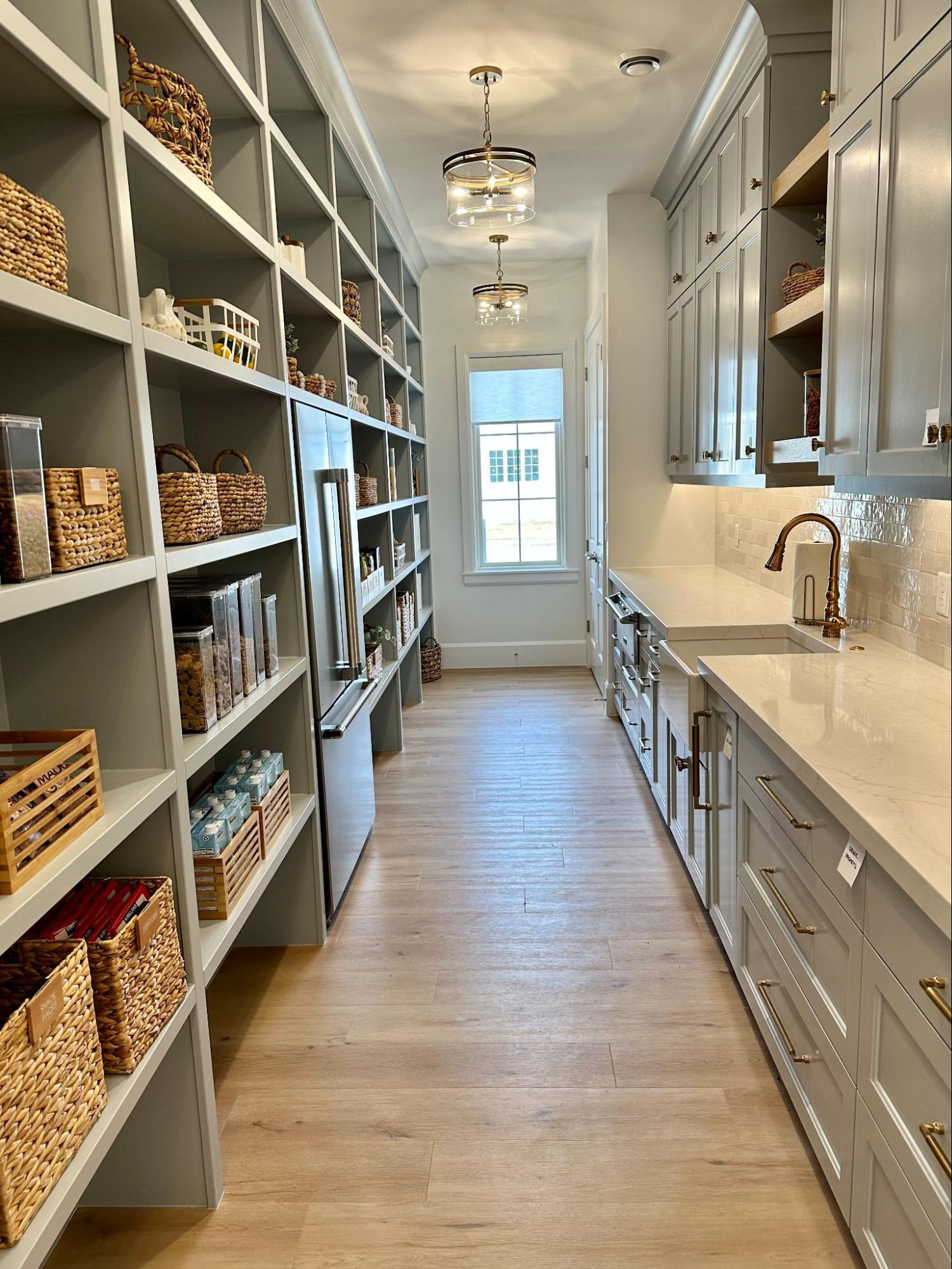 Organized pantry with open shelving, woven storage baskets, labeled containers, and a long countertop workspace