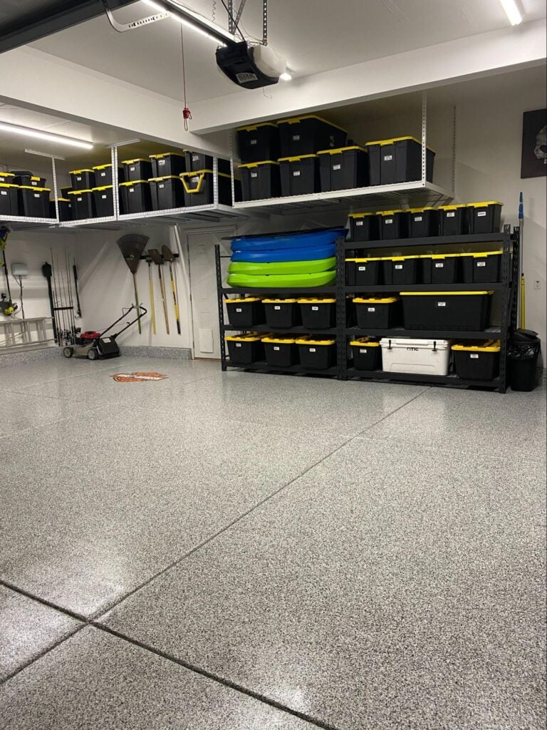 Garage with overhead storage racks holding labeled bins, wall shelving, and organized tools on a clean epoxy floor.
