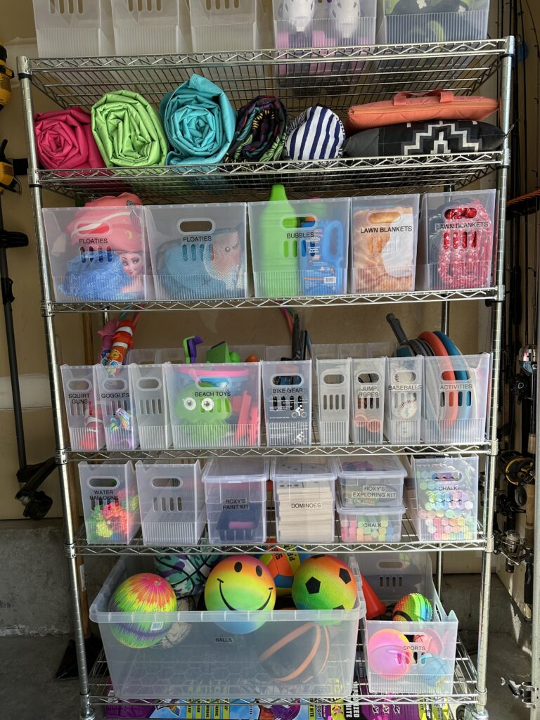 Garage shelving with labeled bins, rolled towels, and neatly organized toys and sports equipment.