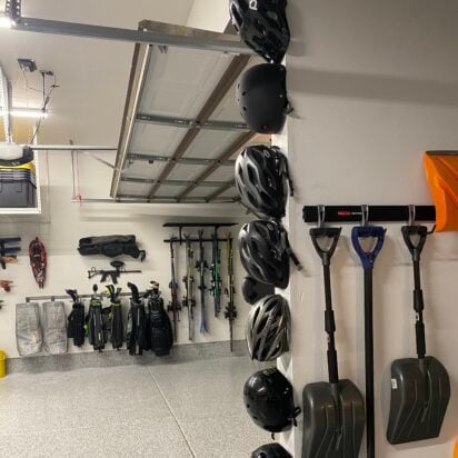 Organized garage wall with mounted helmets, snow shovels, and sports gear on racks, with clean epoxy flooring.