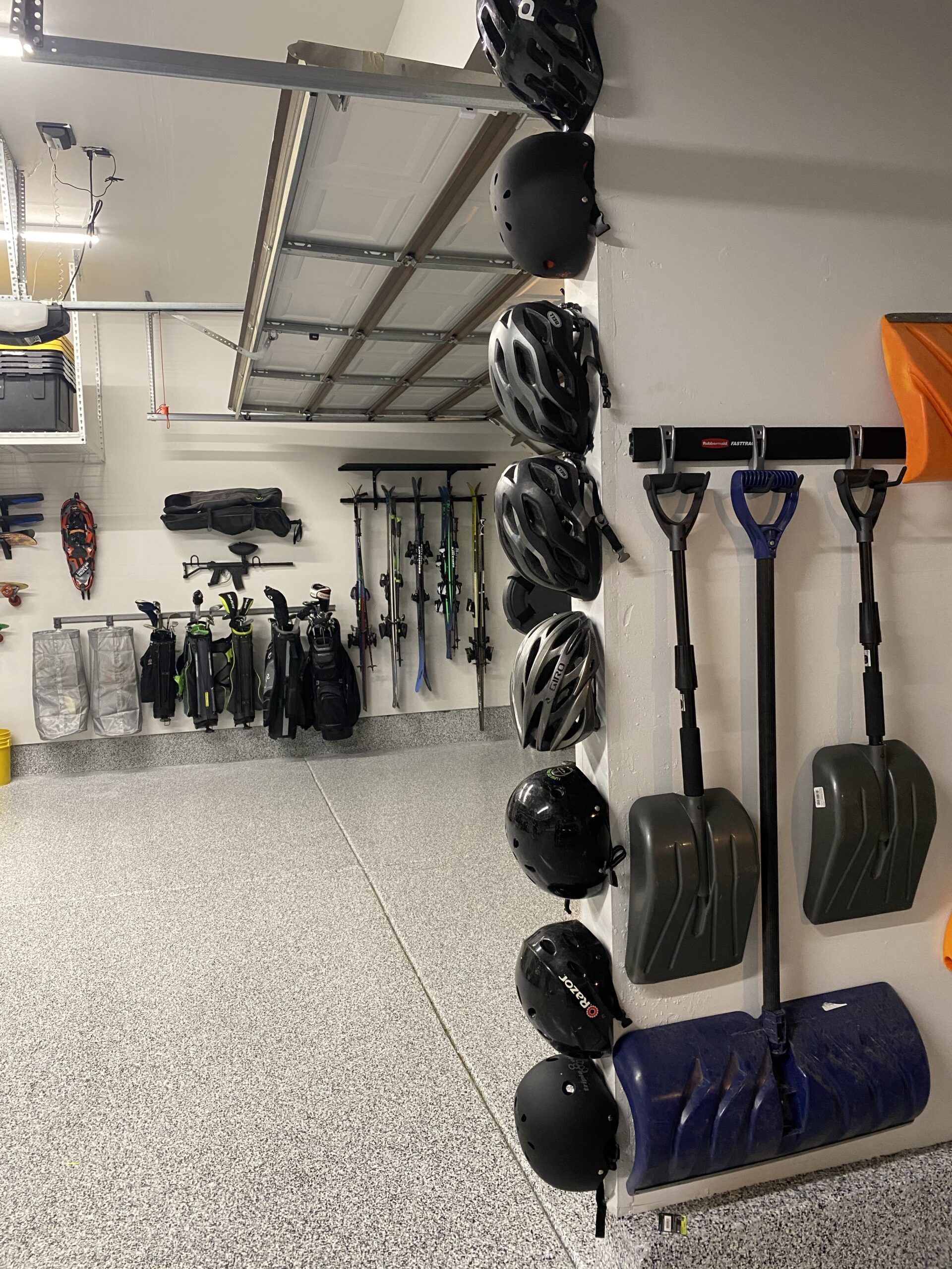 Organized garage wall with mounted helmets, snow shovels, and sports gear on racks, with clean epoxy flooring.