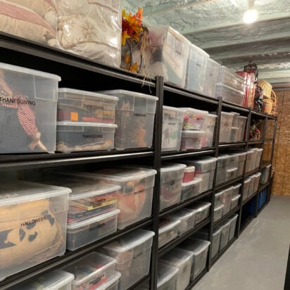 Organized basement storage room with black metal shelving and labeled clear plastic bins for Halloween, Thanksgiving, and Christmas decorations.