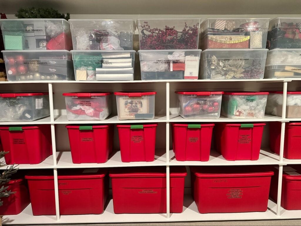 White basement shelving filled with clear plastic storage bins and matching red totes for seasonal decorations.
