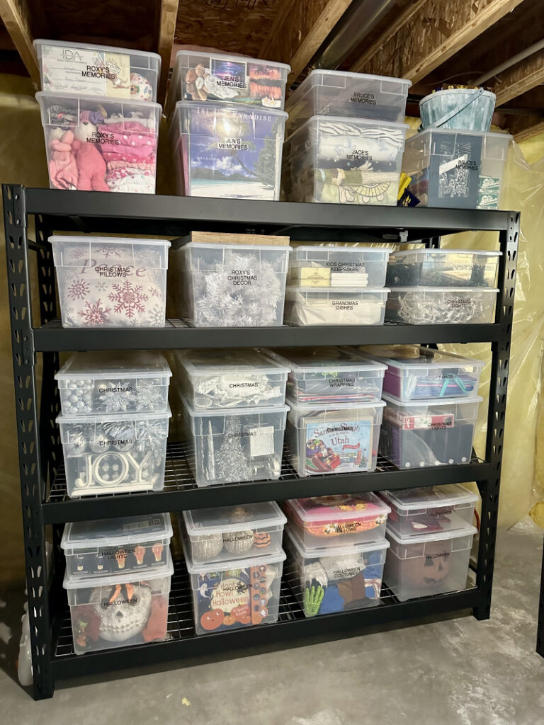 Black shelving unit with clear plastic bins organized by category in an unfinished basement.