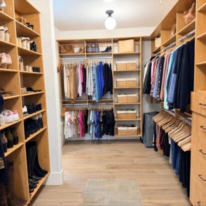 Spacious walk-in closet with natural wood shelving, organized hanging clothes, shoe storage, and built-in drawers.