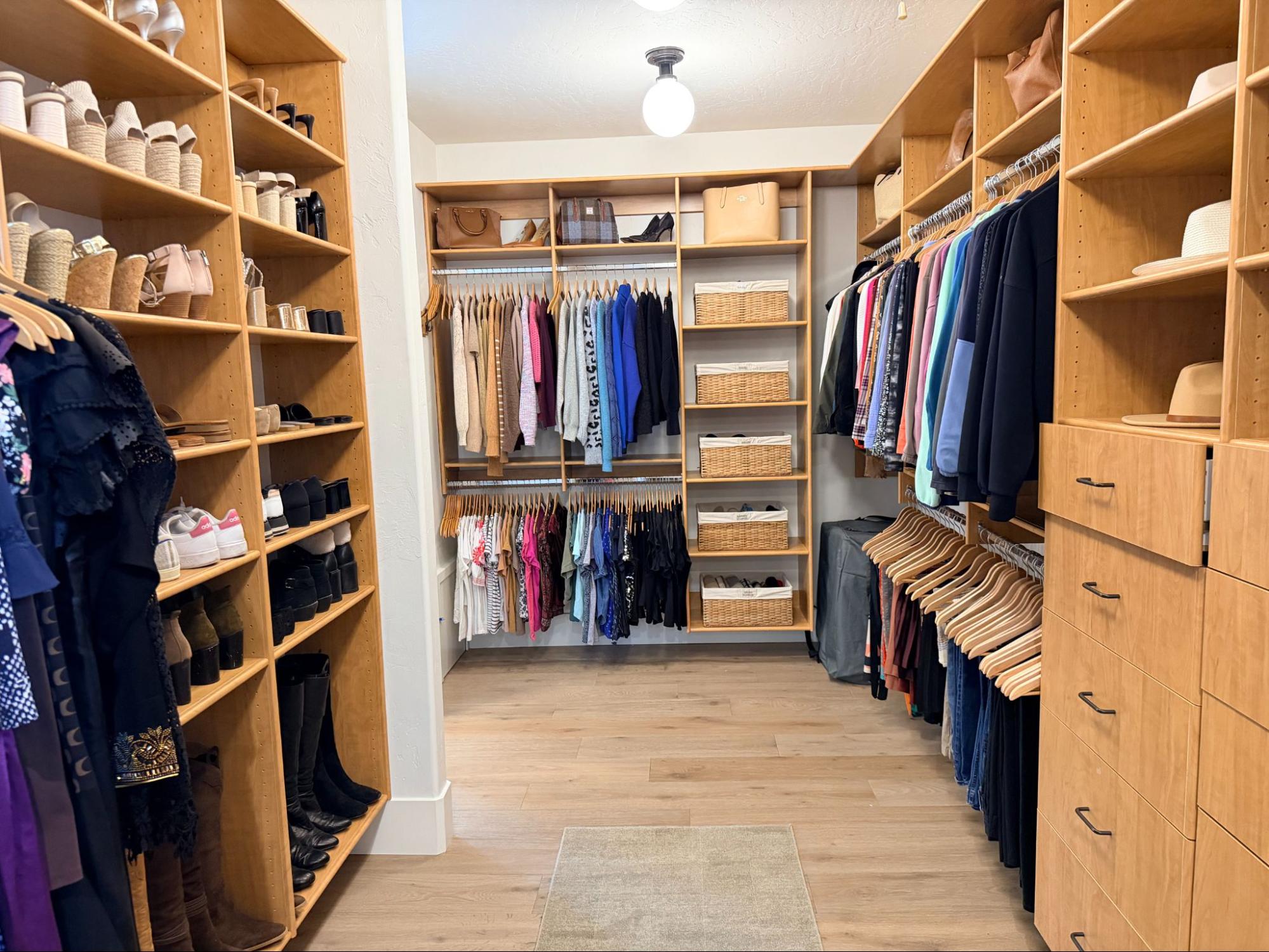 Spacious walk-in closet with natural wood shelving, organized hanging clothes, shoe storage, and built-in drawers.
