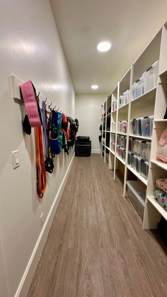 Narrow basement storage room with white built-in shelves and hanging accessories along the opposite wall.